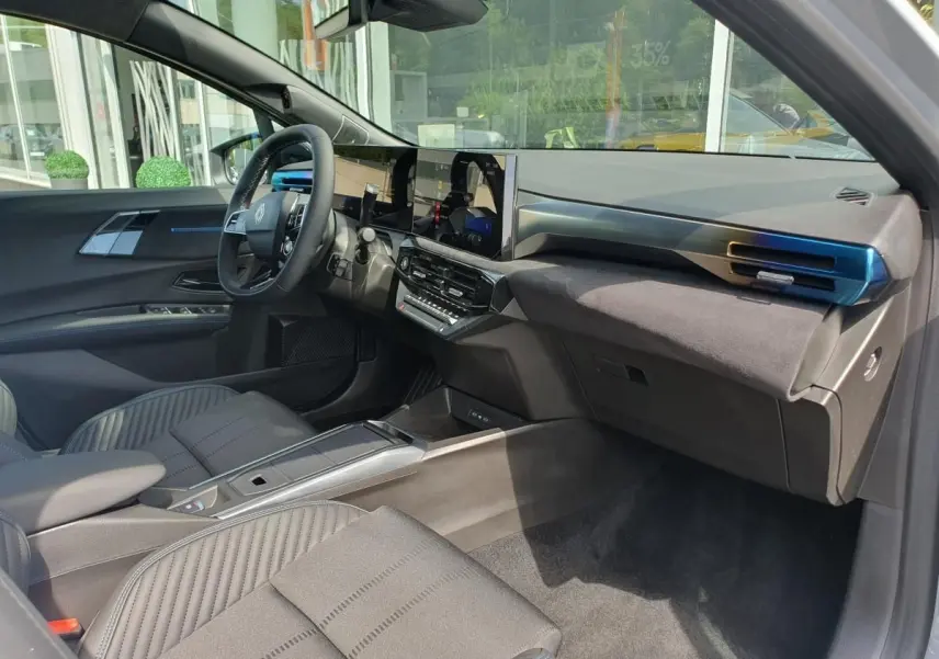 Vue intérieure côté conducteur de la Renault Clio VI hybride 2026, tableau de bord moderne et sièges gris raffinés.