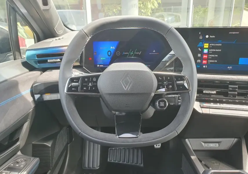 Vue intérieure centrée sur le volant noir avec logo Renault, tableau de bord numérique et écran tactile à droite.