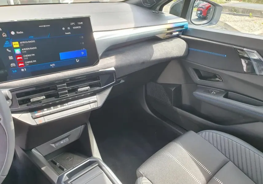 Vue intérieure côté passager de la Renault Clio VI gris Rafale, avec écran tactile et finitions bleues sur la porte.