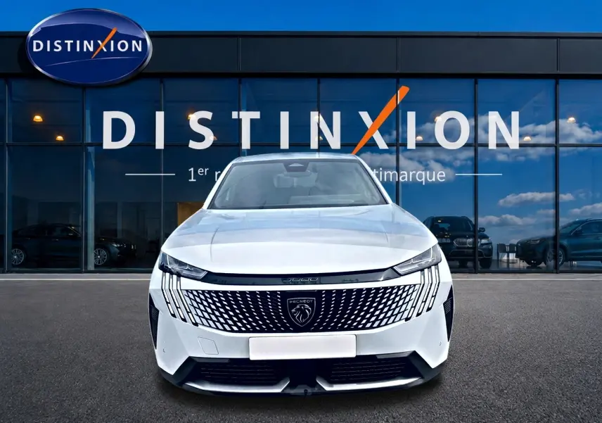Vue frontale d'un Peugeot 3008 blanc 2025 avec calandre distinctive et phares LED fins, devant une vitrine Distinxion.