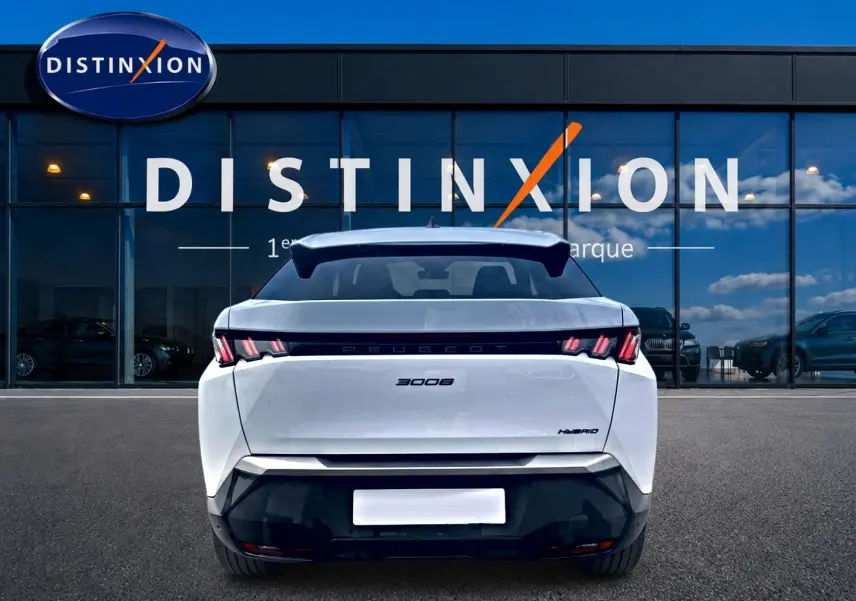 Vue arrière d'un Peugeot 3008 blanc hybride 2025, avec becquet arrière et feux LED distinctifs, devant une vitrine Distinxion.