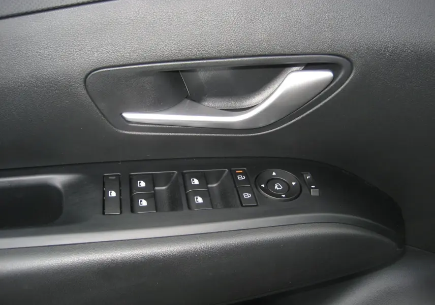 Gros plan sur la poignée de porte intérieure et les commandes des vitres du côté conducteur d'un Hyundai Tucson gris Ecotronic 2025.