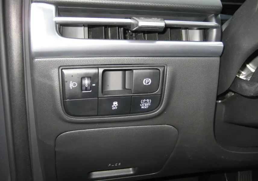 Vue rapprochée du tableau de bord côté gauche du Hyundai Tucson 2025 gris Ecotronic, montrant les commandes d'éclairage et frein à main électrique.