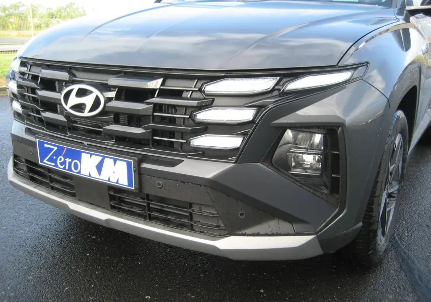 Vue de face droite du Hyundai Tucson 2025 gris Ecotronic avec calandre imposante et feux LED distinctifs allumés.