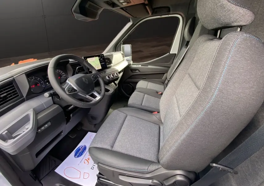 Vue intérieure côté conducteur du Renault Master 2025, sièges gris avec surpiqûres bleues et tableau de bord moderne noir et gris.