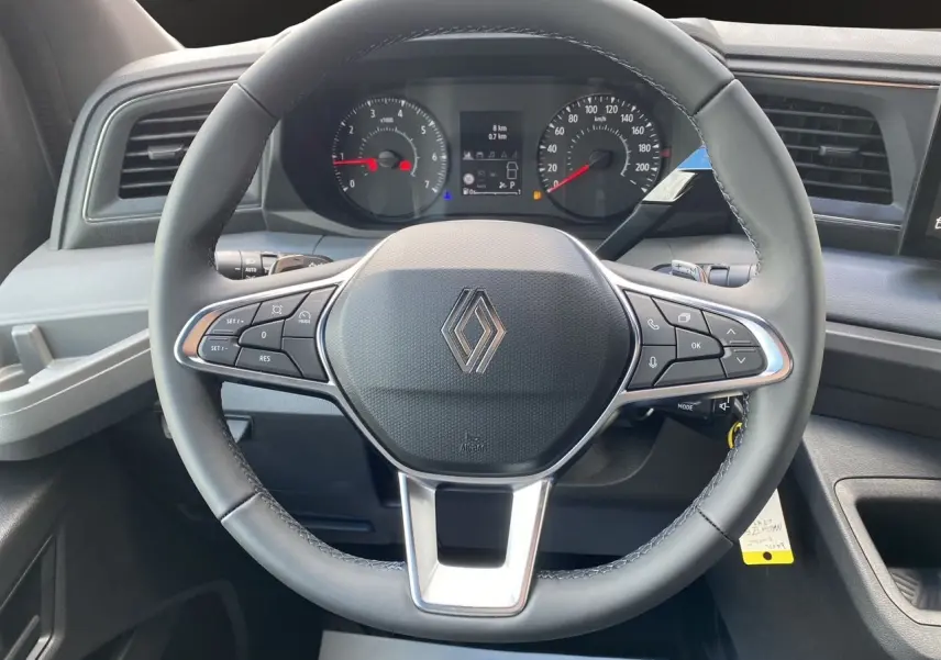 Vue rapprochée du volant noir du Renault Master 2025 avec commandes intégrées et tableau de bord numérique en arrière-plan.