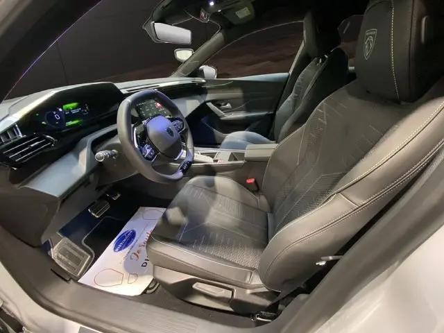 Intérieur avant droit de la Peugeot 308 hybride blanche, siège en tissu noir avec logo Peugeot brodé, tableau de bord digital.