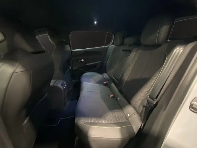 Vue intérieure arrière côté droit de la Peugeot 308 hybride blanche, montrant les sièges arrière en cuir noir avec surpiqûres.
