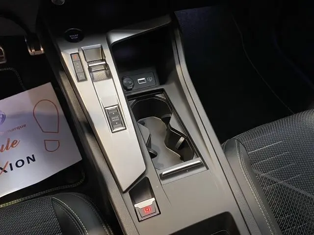 Vue rapprochée de la console centrale de la Peugeot 308 hybride blanche, avec commandes de boîte auto et porte-gobelets.