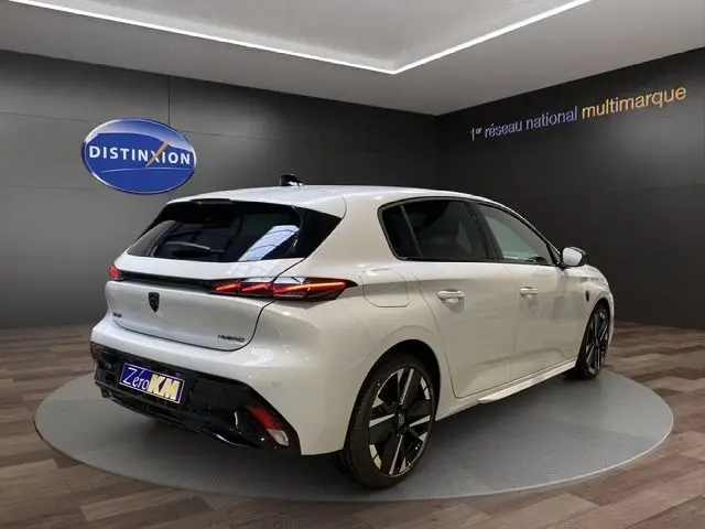 Vue 3/4 arrière droite de la Peugeot 308 blanche Okenite, nouvelle hybrid 145 GT avec jantes noires et toit noir.