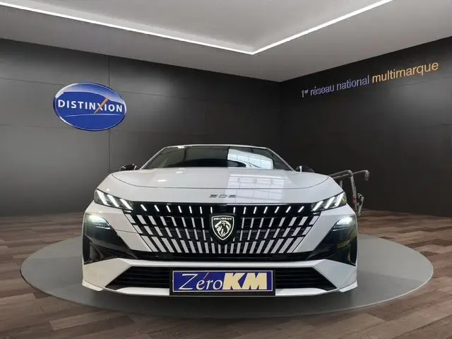 Vue frontale d'une Peugeot 308 blanche Okenite 2026 avec calandre distinctive et éclairage LED en showroom.