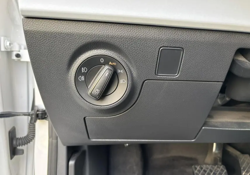 Gros plan sur le bouton de commande des phares à gauche du tableau de bord d'un SEAT Arona blanc, intérieur noir.