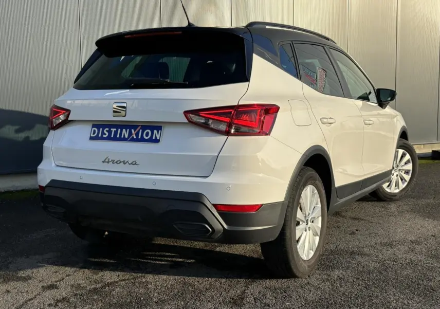 Vue 3/4 arrière droite d'un SEAT Arona blanc avec toit noir et jantes alliage 16 pouces, stationné sur sol asphalté.