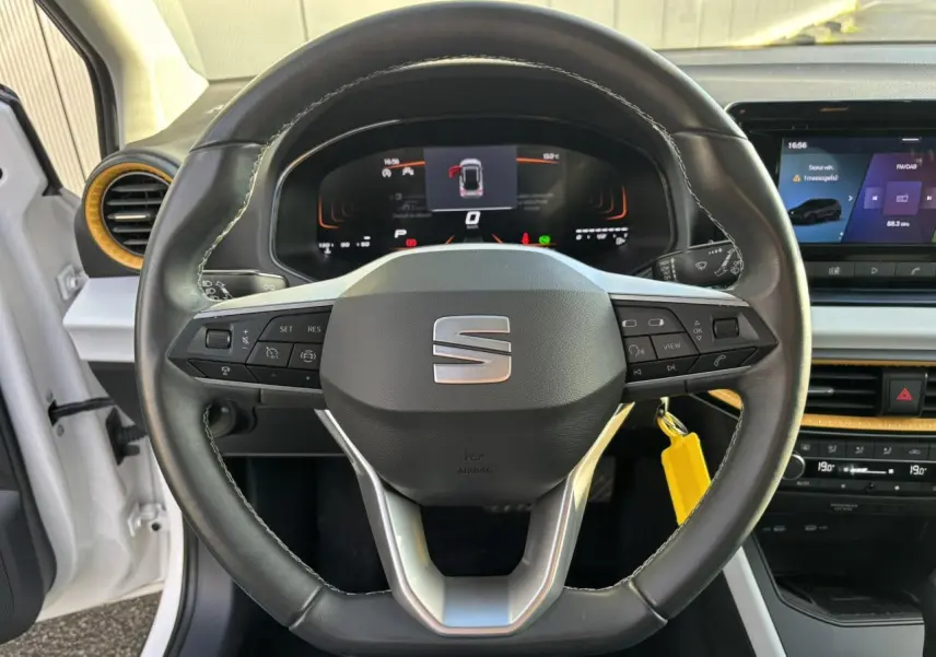 Vue intérieure centrée sur le volant noir du SEAT Arona blanc avec tableau de bord digital et écran tactile.