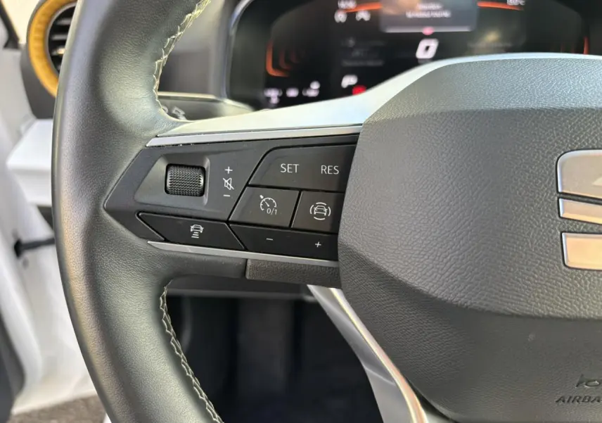 Gros plan sur le volant noir du SEAT Arona blanc, mettant en valeur les commandes de régulateur de vitesse à gauche.