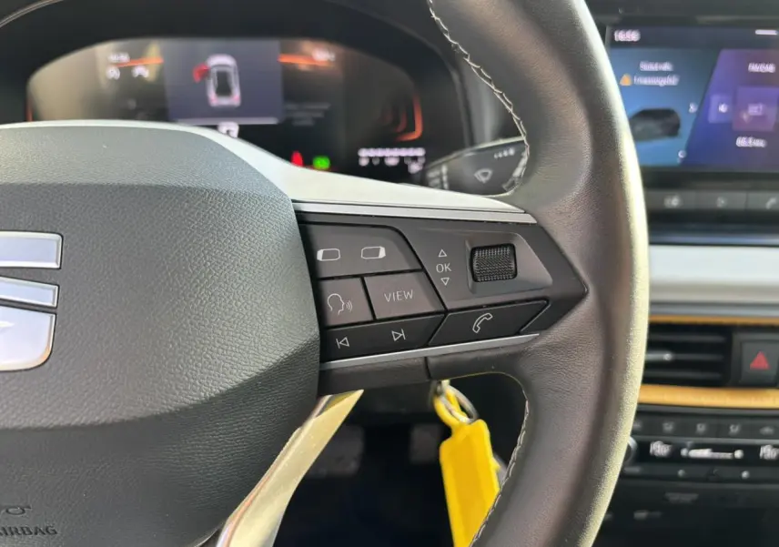 Gros plan sur le volant côté droit du SEAT Arona blanc 2025 avec commandes multimédia et tableau de bord digital flou.