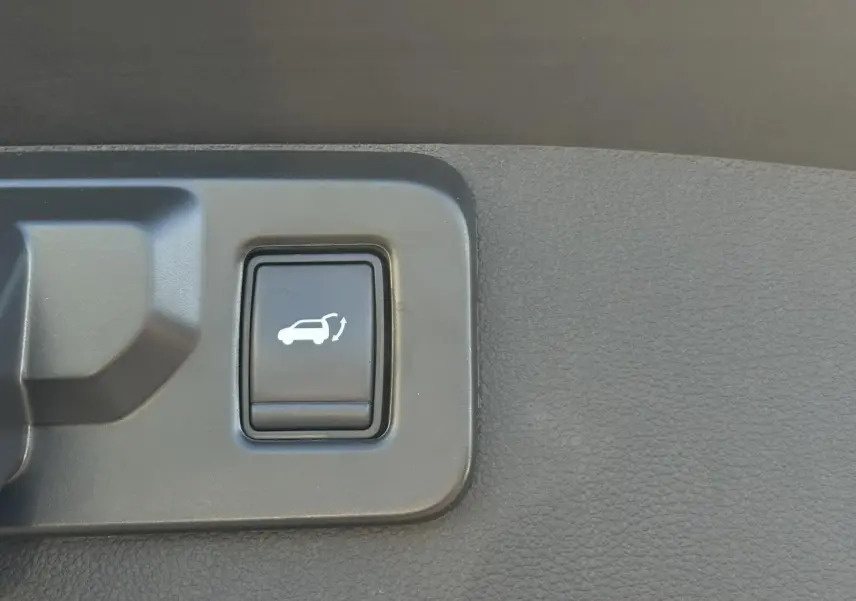 Gros plan sur le bouton d'ouverture électrique du hayon dans l'habitacle du Renault Symbioz gris Cassiopée.