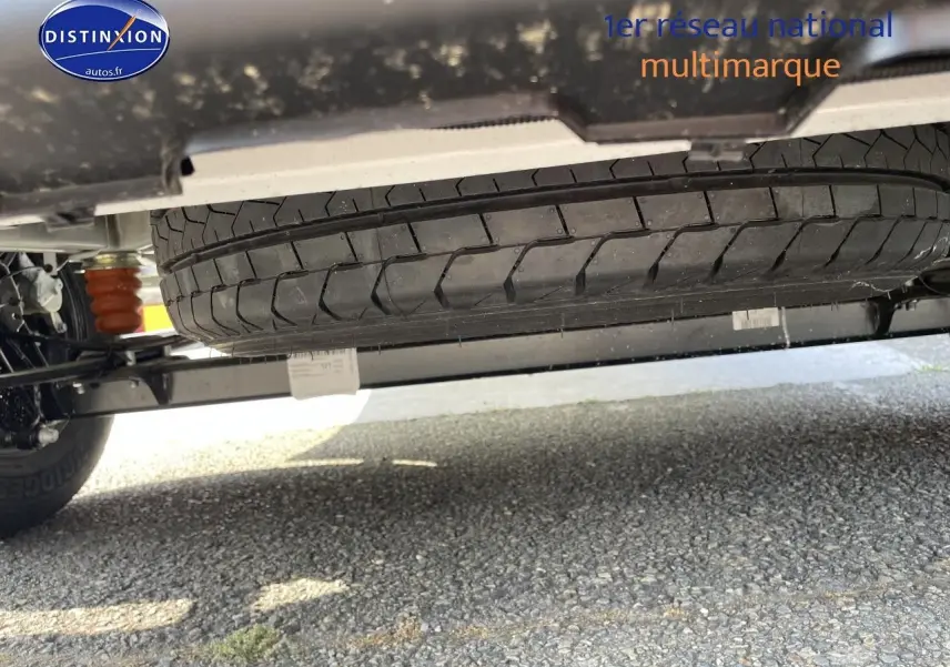 Vue en contre-plongée sous un Peugeot Boxer Fourgon blanc, mettant en valeur la roue de secours et le châssis.