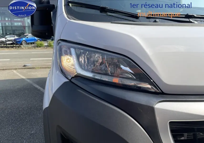 Gros plan sur le phare avant gauche allumé du Peugeot Boxer Fourgon blanc, avec pare-chocs noir visible.