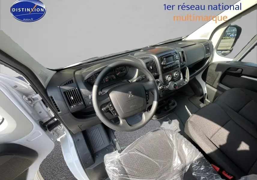 Vue intérieure côté conducteur du Peugeot Boxer Fourgon blanc 2023, tableau de bord et volant visibles, siège protégé par une housse plastique.