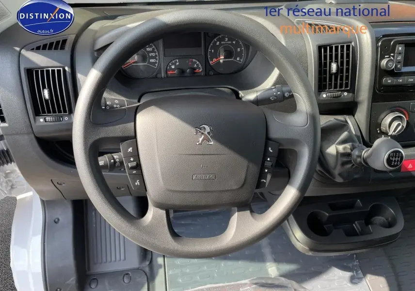 Vue intérieure centrée sur le volant noir du Peugeot Boxer Fourgon blanc, avec tableau de bord et levier de vitesses manuelle visibles.