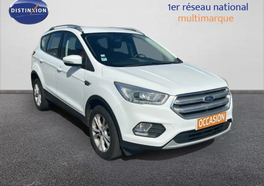 Ford Kuga blanc en 3/4 avant droit avec barres de toit et jantes alliage 17 pouces visible sur sol gris.