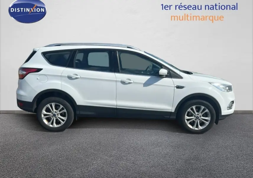 Ford Kuga blanc en profil droit, avec barres de toit et jantes alliage 17 pouces visibles.
