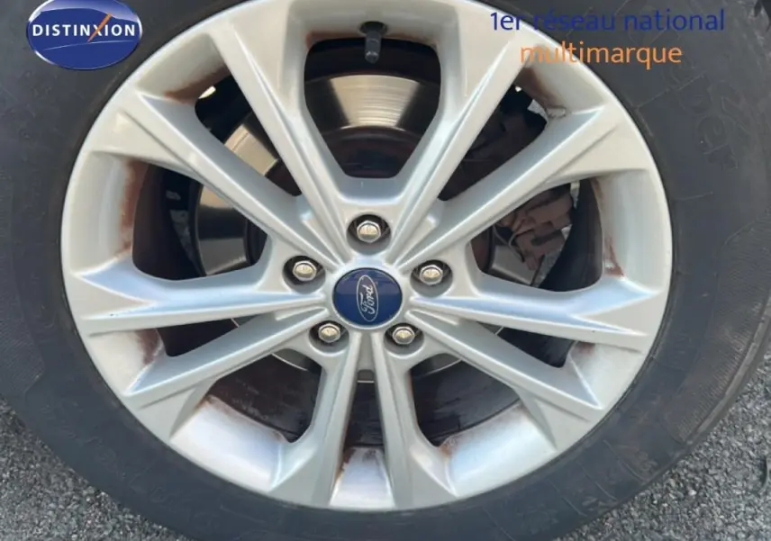 Gros plan sur la jante alliage 17 pouces argentée d’un Ford Kuga blanc avec logo Ford au centre.