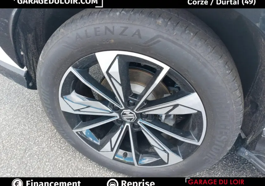 Gros plan sur la jante noire et argentée du MG MOTOR EHS 2025 avec logo MG au centre, pneu Bridgestone visible.