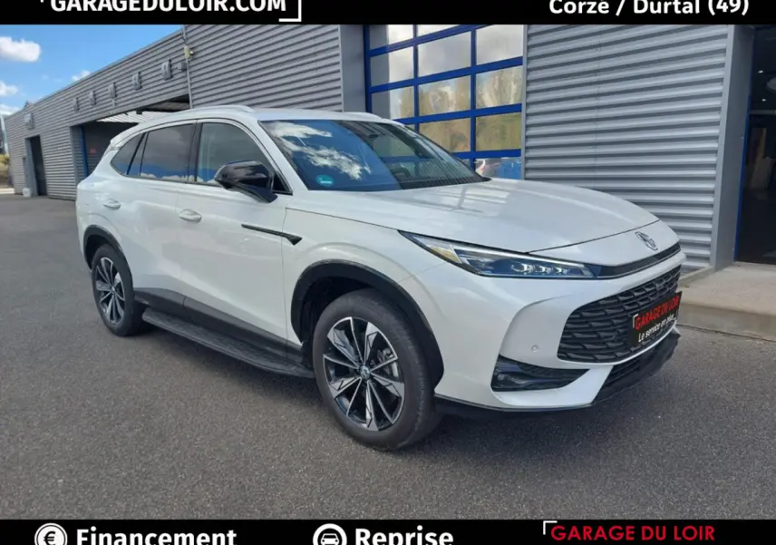 MG Motor EHS hybride rechargeable blanc, vue 3/4 avant droit devant un bâtiment industriel.
