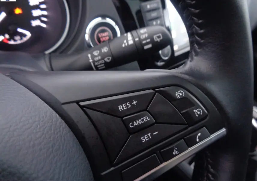 Gros plan sur les commandes au volant noir du Nissan Qashqai blanc lunaire, mettant en valeur les boutons de régulateur de vitesse.