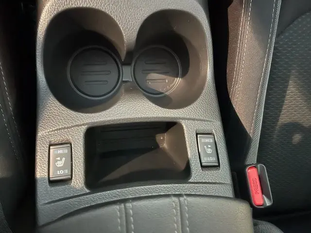 Vue rapprochée de la console centrale noire du Nissan Qashqai avec commandes de sièges chauffants et porte-gobelets.