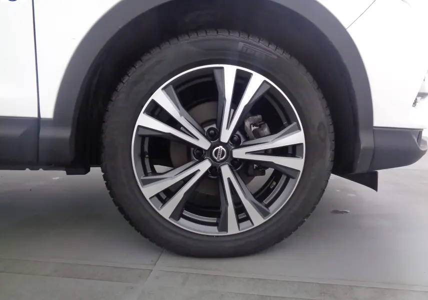 Gros plan sur la roue avant droite du Nissan Qashqai blanc lunaire métal, mettant en valeur la jante alliage moderne.