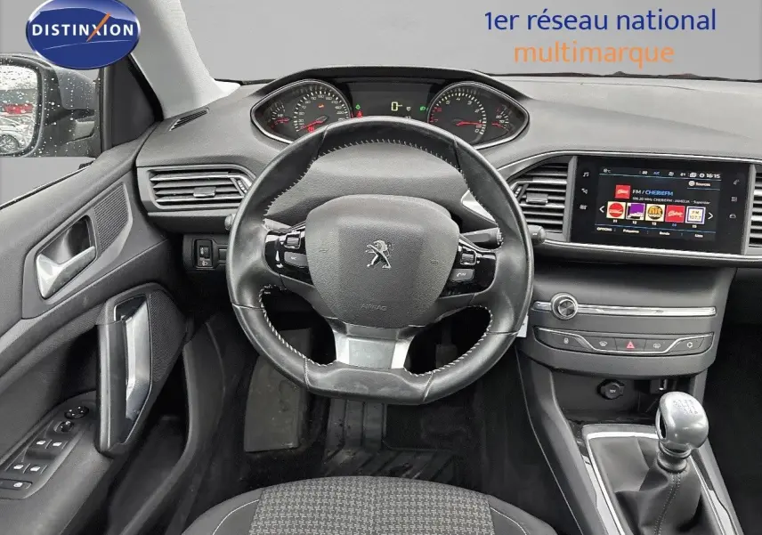 Vue intérieure avant de la Peugeot 308 gris Artense de 2019, tableau de bord avec volant cuir et boîte manuelle visible.
