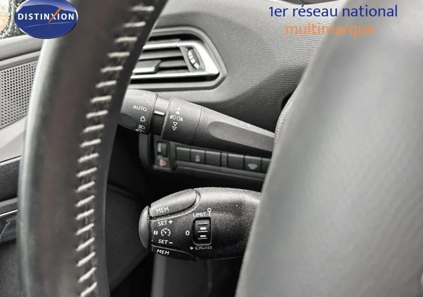 Gros plan sur la commande de régulateur de vitesse derrière le volant d'une Peugeot 308 gris Artense, intérieur noir.