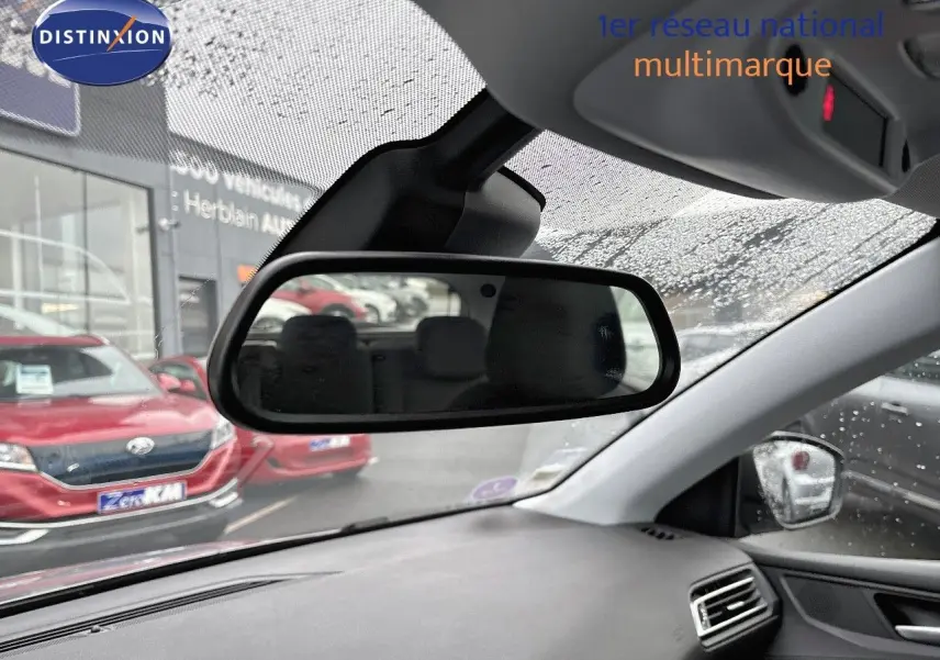 Vue intérieure du rétroviseur central d'une Peugeot 308 gris Artense, avec tableau de bord et pluie sur le pare-brise visible.