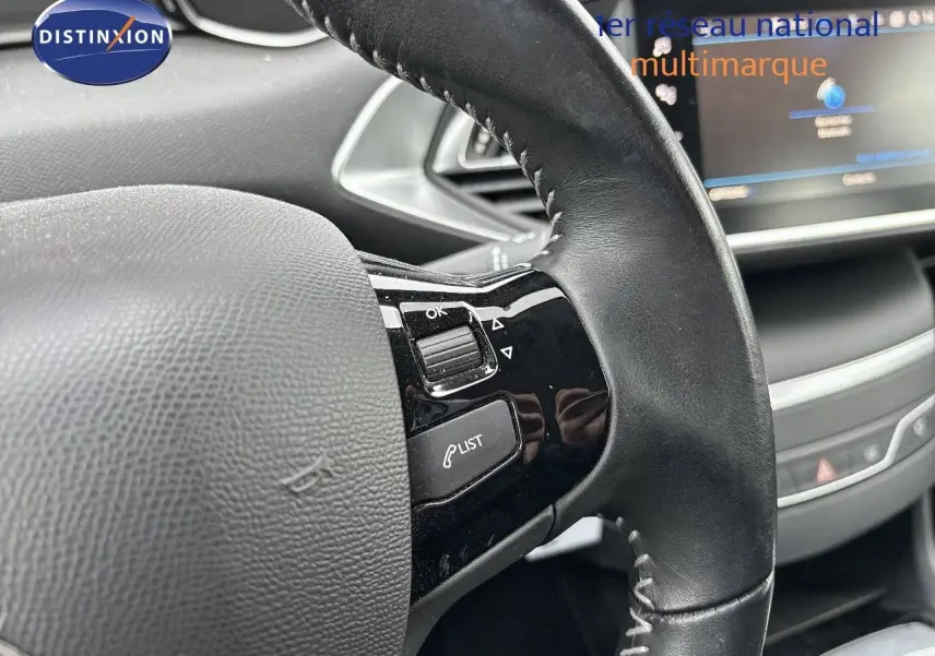 Gros plan sur le volant en cuir noir de la Peugeot 308 gris Artense, avec commandes intégrées visibles côté gauche.