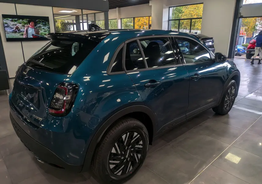 Vue 3/4 arrière droite d'une FIAT 600 hybride bleu Sea en showroom, avec jantes noires et toit noir brillant.