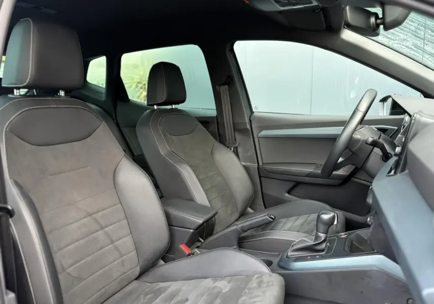Vue intérieure côté conducteur du SEAT Arona 2025, sièges en cuir et alcantara gris avec console centrale et volant visibles.
