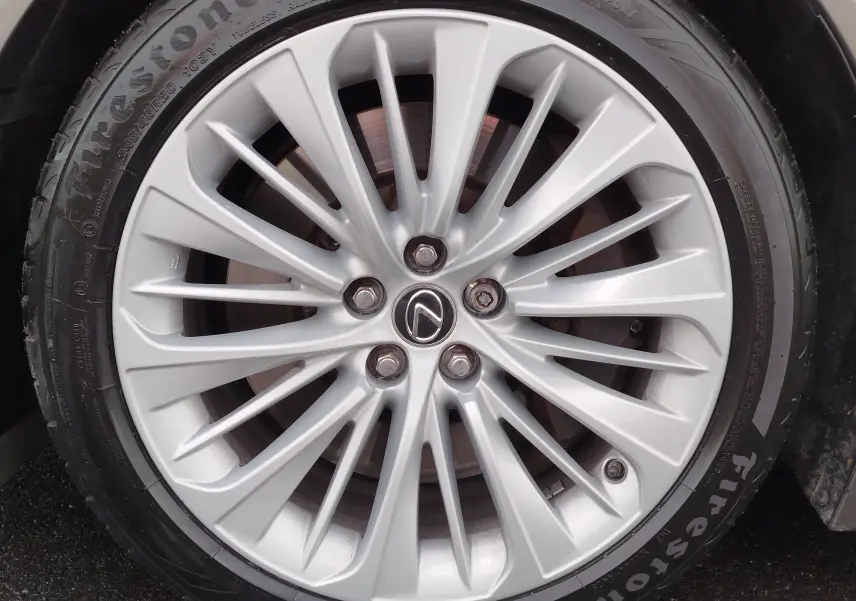 Gros plan sur la jante argentée en alliage avec logo Lexus au centre, montée sur pneu Firestone.