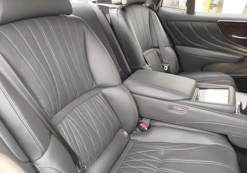 Vue intérieure des sièges arrière en cuir noir perforé avec surpiqûres blanches et accoudoir central sur Lexus LS 500H 2020.