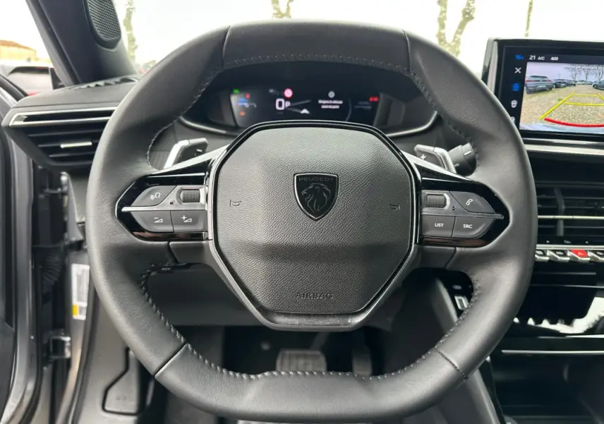Vue rapprochée du volant cuir noir du Peugeot 2008 Hybrid 145 e-DCS6 Allure 2025 avec tableau de bord numérique et écran tactile.