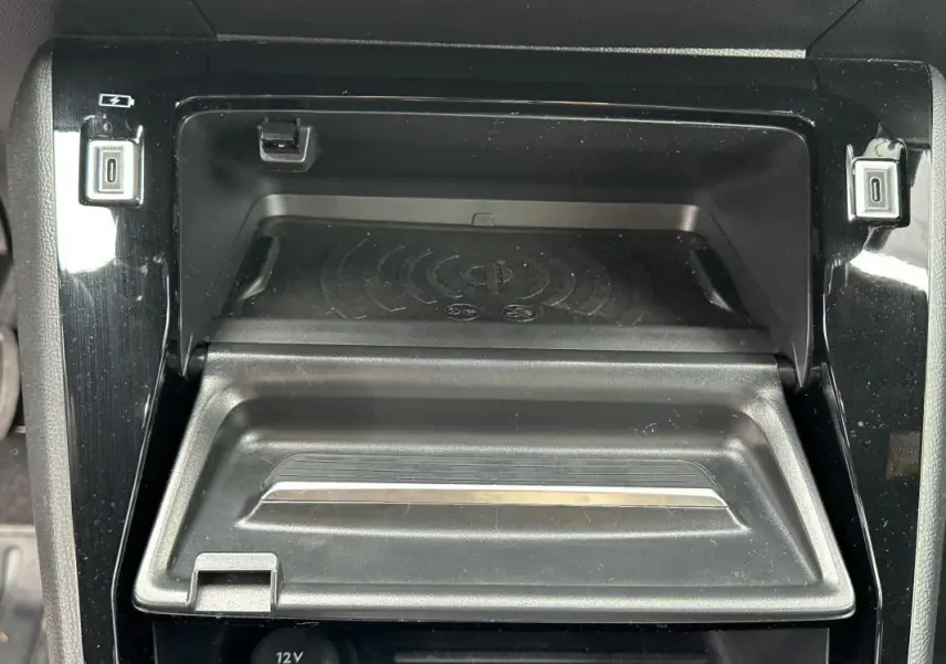 Gros plan sur la console centrale noire du Peugeot 2008 Hybrid 145, montrant le compartiment de recharge sans fil et ports USB.