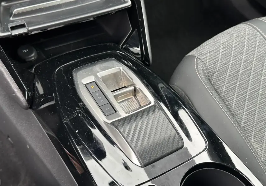 Vue rapprochée de la console centrale noire brillante avec levier de vitesse automatique et siège gris à motifs du Peugeot 2008 Hybrid 145.