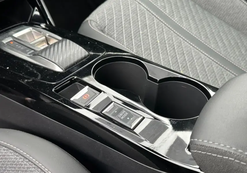 Gros plan sur la console centrale noire brillante du Peugeot 2008 Hybrid 145 Allure avec commandes de frein à main et mode de conduite.