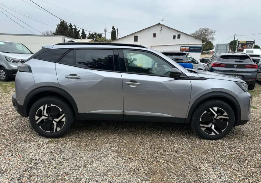 Profil côté gauche du Peugeot 2008 Hybrid 145 e-DCS6 Allure gris avec jantes alliage 17 pouces sur sol gravillonné.