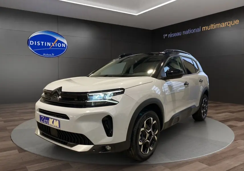 Vue 3/4 avant d'un Citroën C5 Aircross blanc avec toit noir et jantes alliage, en showroom intérieur.