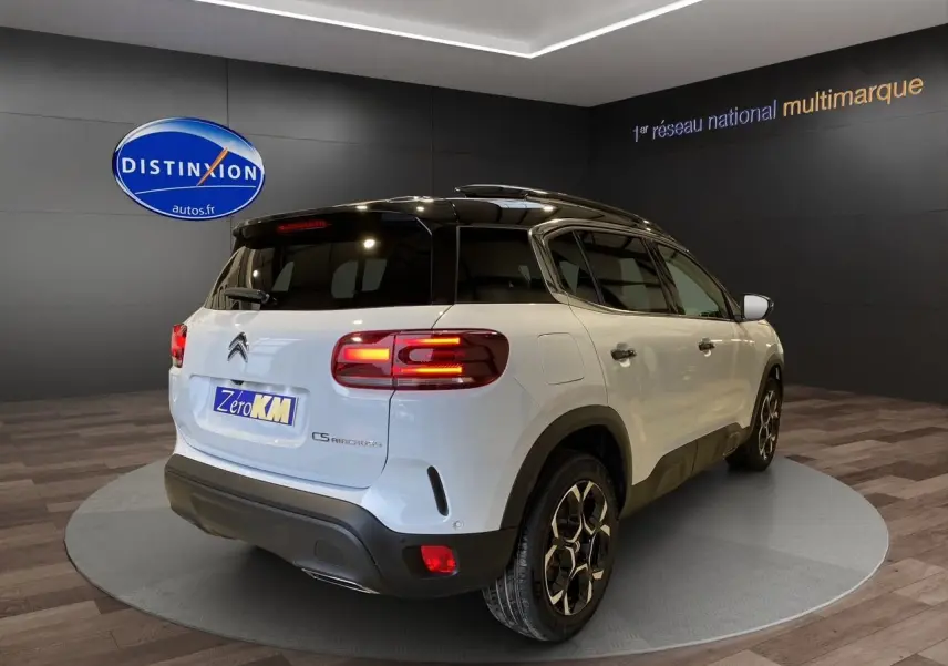 Vue 3/4 arrière droite d'un Citroën C5 Aircross blanc avec toit noir et feux arrière allumés en showroom.
