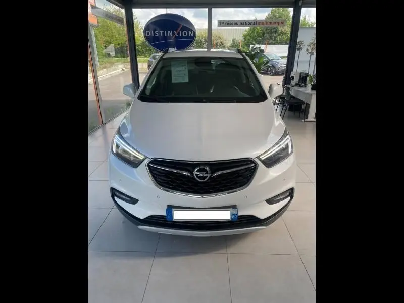 Vue frontale d'un Opel Mokka blanc 2017 exposé en showroom avec calandre noire et phares LED allumés.