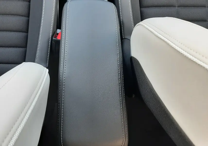 Vue plongeante sur l'accoudoir central noir entre sièges avant bicolores noir et blanc du Citroën C3 Aircross hybride 2026.